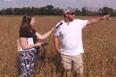A female student interviews a male in a farm field.